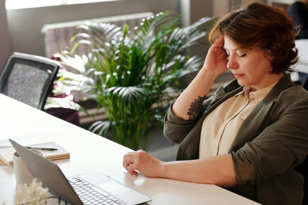 A woman having head chronic pains as a caregiver, while doing paperwork on her desk.