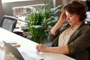 A woman having head chronic pains as a caregiver, while doing paperwork on her desk.