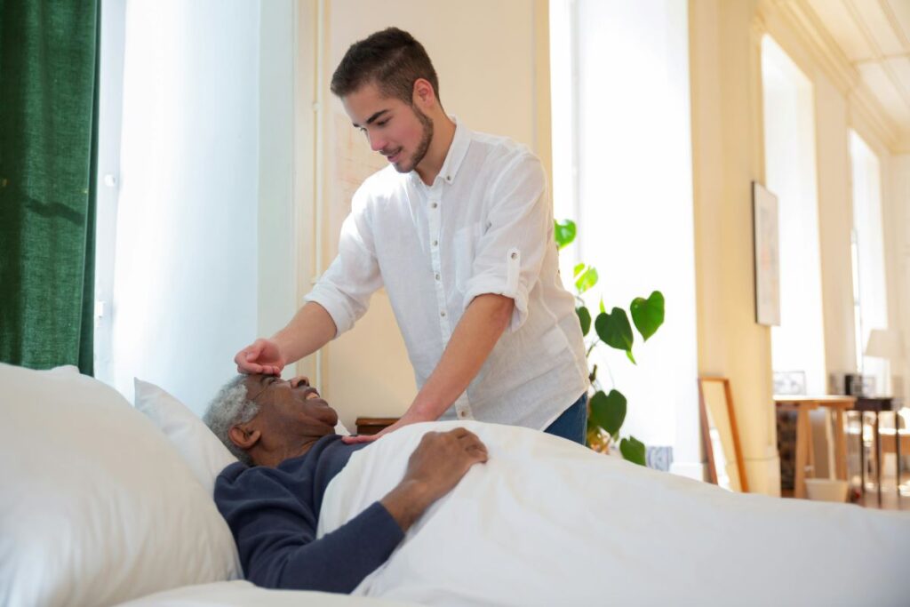 Daily responsibilities of a caregiver as seen in this image showing a man in white caring for an elderly in bed | Photo by Kampus Production