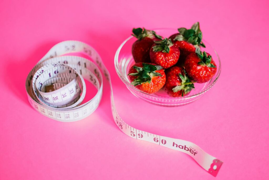 Rolled-up measuring tape beside a bowl of strawberries.