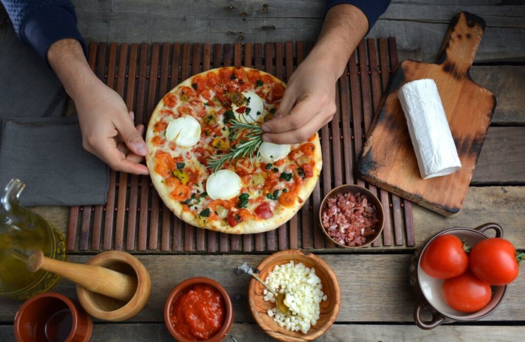 A person adding toppings to a pizza, emphasizing the process of creating authentic Italian pizza recipes.