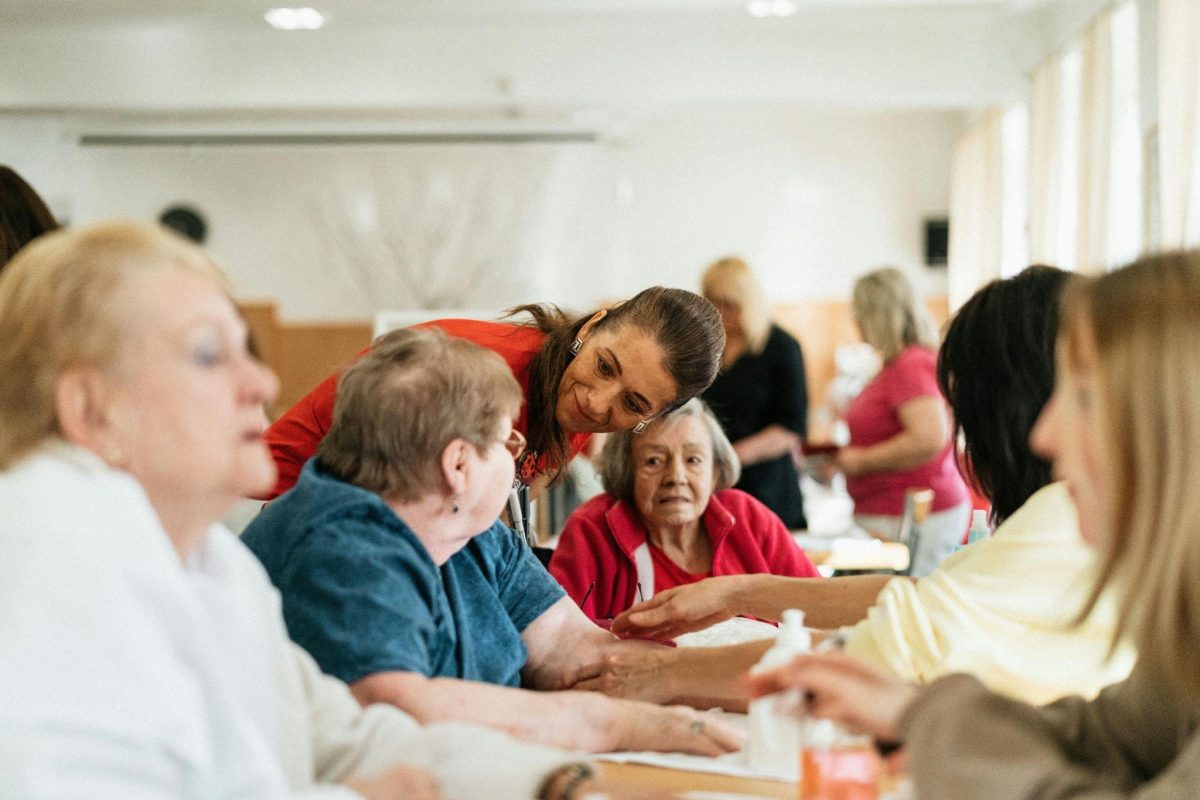 A caregiver helps an elderly woman at a table, illustrating how social activities help caregivers overcome isolation.