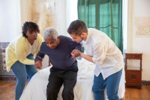 Caregivers help an elderly man in bed, highlighting support for managing chronic conditions in seniors.