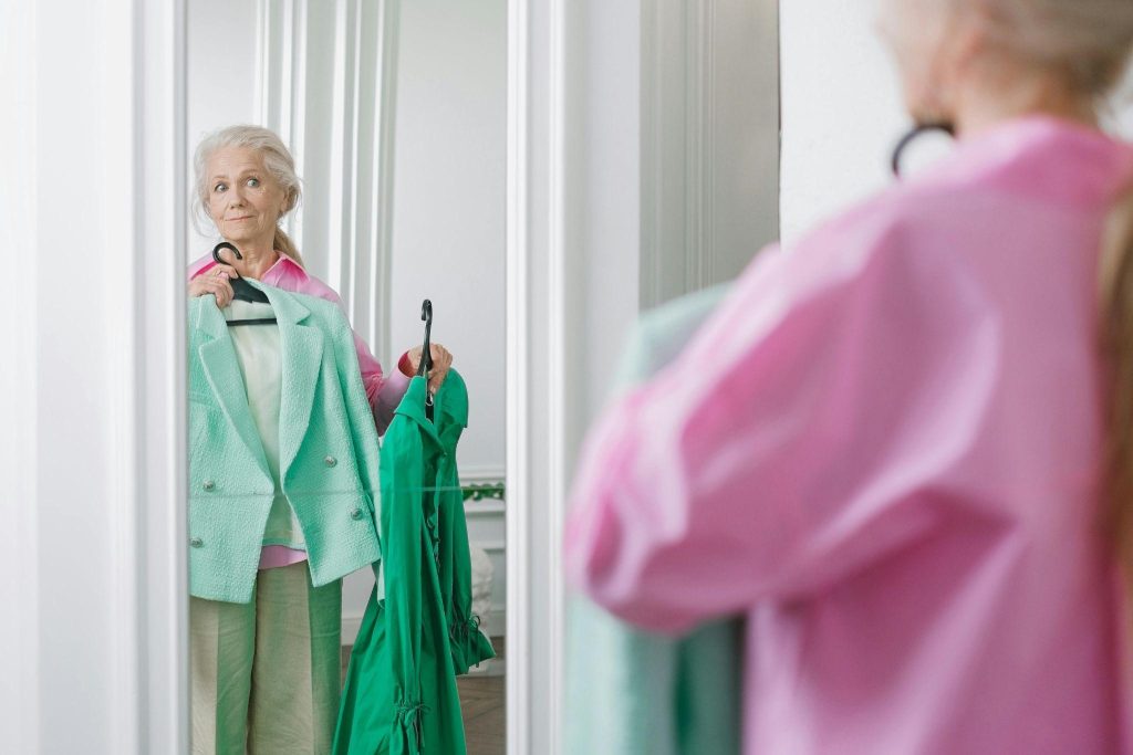 An elderly person in front of a mirror, holding up a blouse, symbolizing how caregivers should respond when a dementia patient talks to themselves.