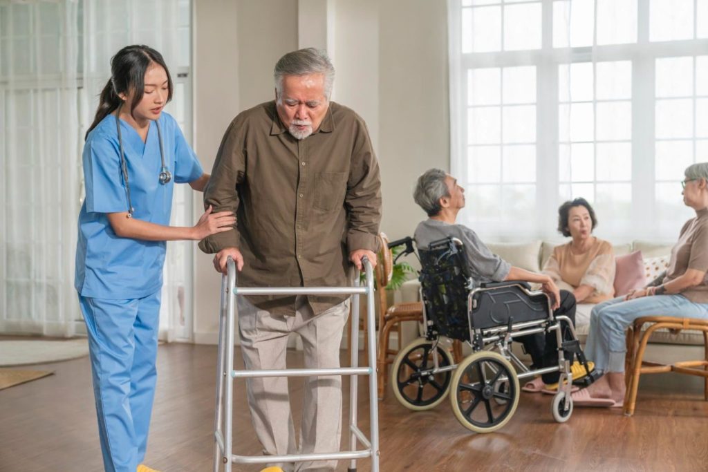 A caregiver helping an old man learn to walk again.