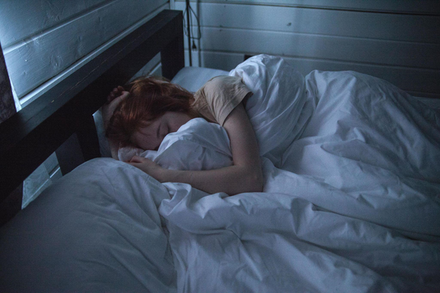 A person sleeps peacefully on a bed, wrapped in white sheets.