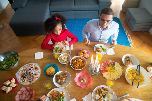 A father and daughter enjoy a meal at a wooden table filled with diverse dishes, salads, and drinks.