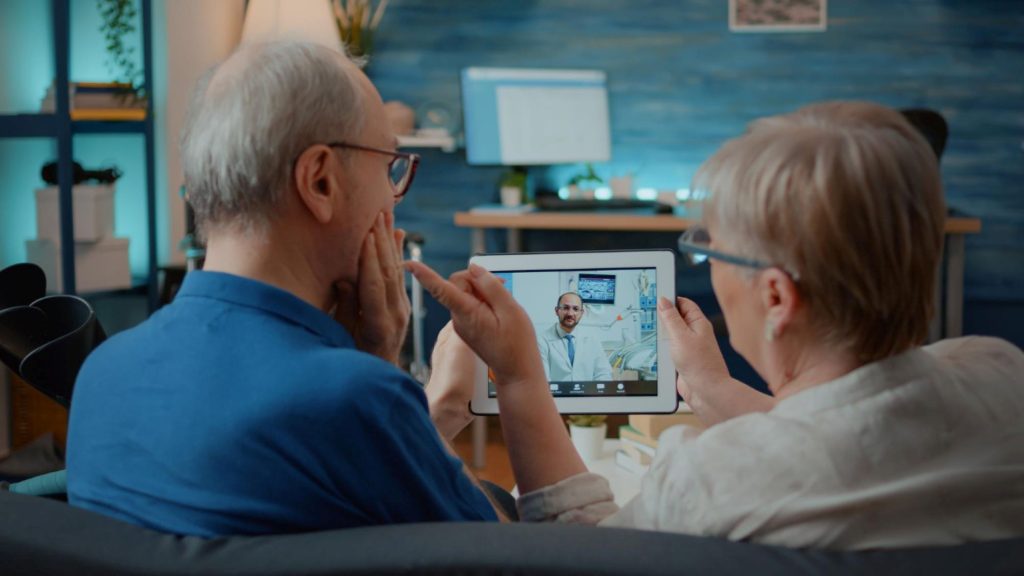 An elderly couple talking to a doctor via teleconferencing.
