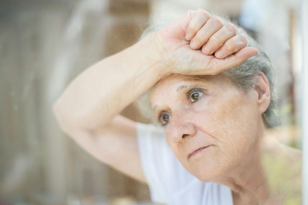 Elderly woman looking thoughtfully out a window, relating to why dementia patients talk to themselves.