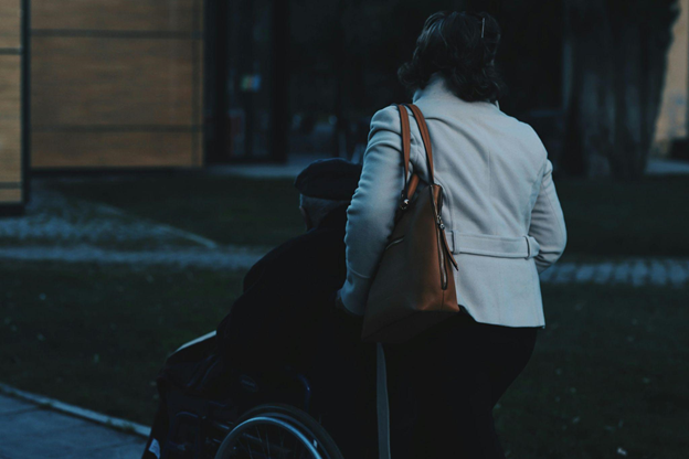 Woman pushing a person in a wheelchair outdoors at dusk.