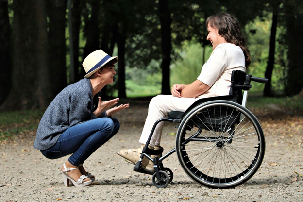 A woman in a wheelchair smiles at the caregiver crouching in front of her.