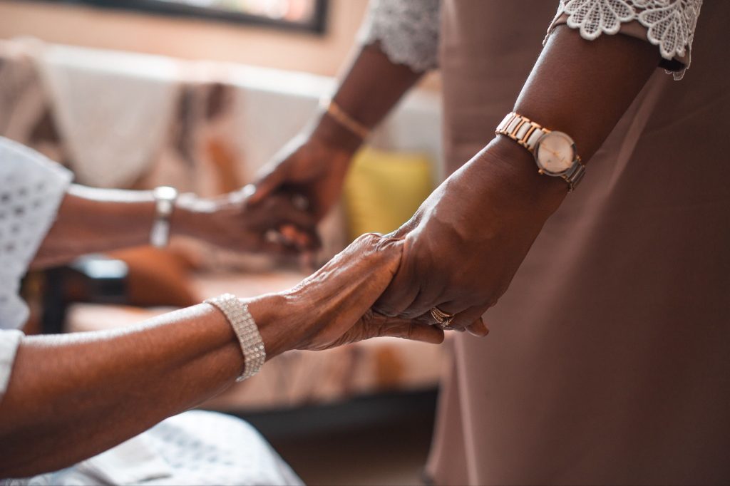 An elderly woman and her caregiver clasp hands, symbolizing the essence of hospice vs palliative care.