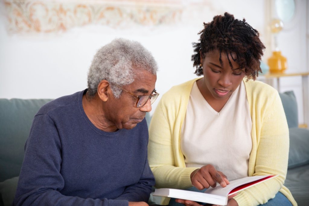 A woman and an elderly man engaged in reading a caregiving education book, fostering learning and understanding.