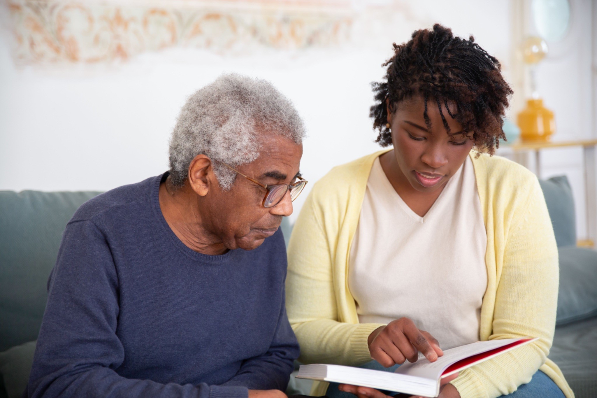 A woman and an elderly man engaged in reading a caregiving education book, fostering learning and understanding.