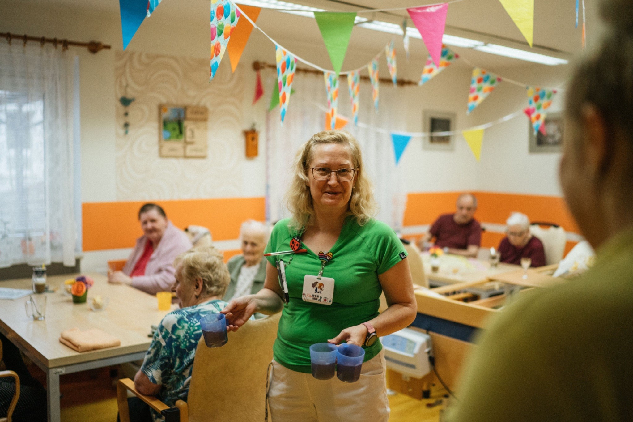 A woman smiles while holding cups of coffee, representing a social moment at an adult daycare program.