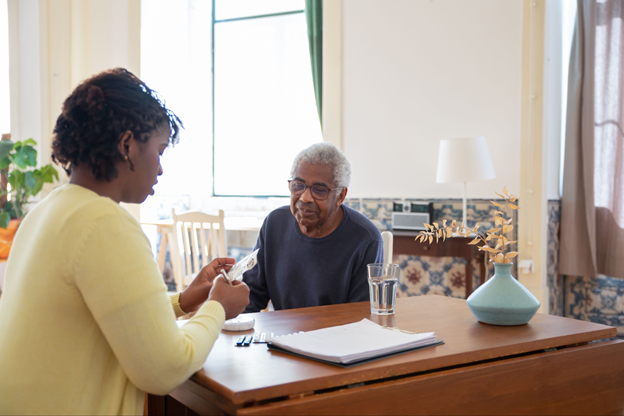 A woman engages in conversation with an older man at a table, highlighting a caregiving interaction.