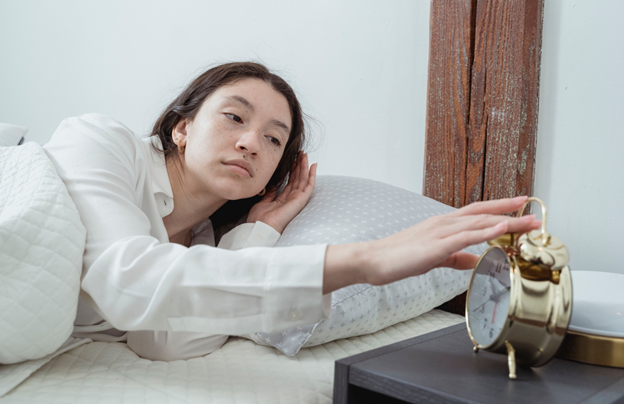 A woman lying in bed next to an alarm clock, appearing relaxed and contemplative.