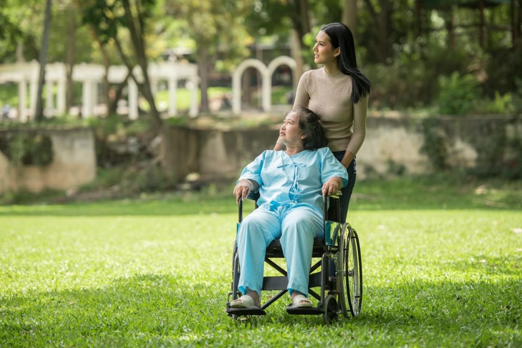 An elderly woman in a wheelchair is accompanied by a woman, symbolizing support in end-of-life care.